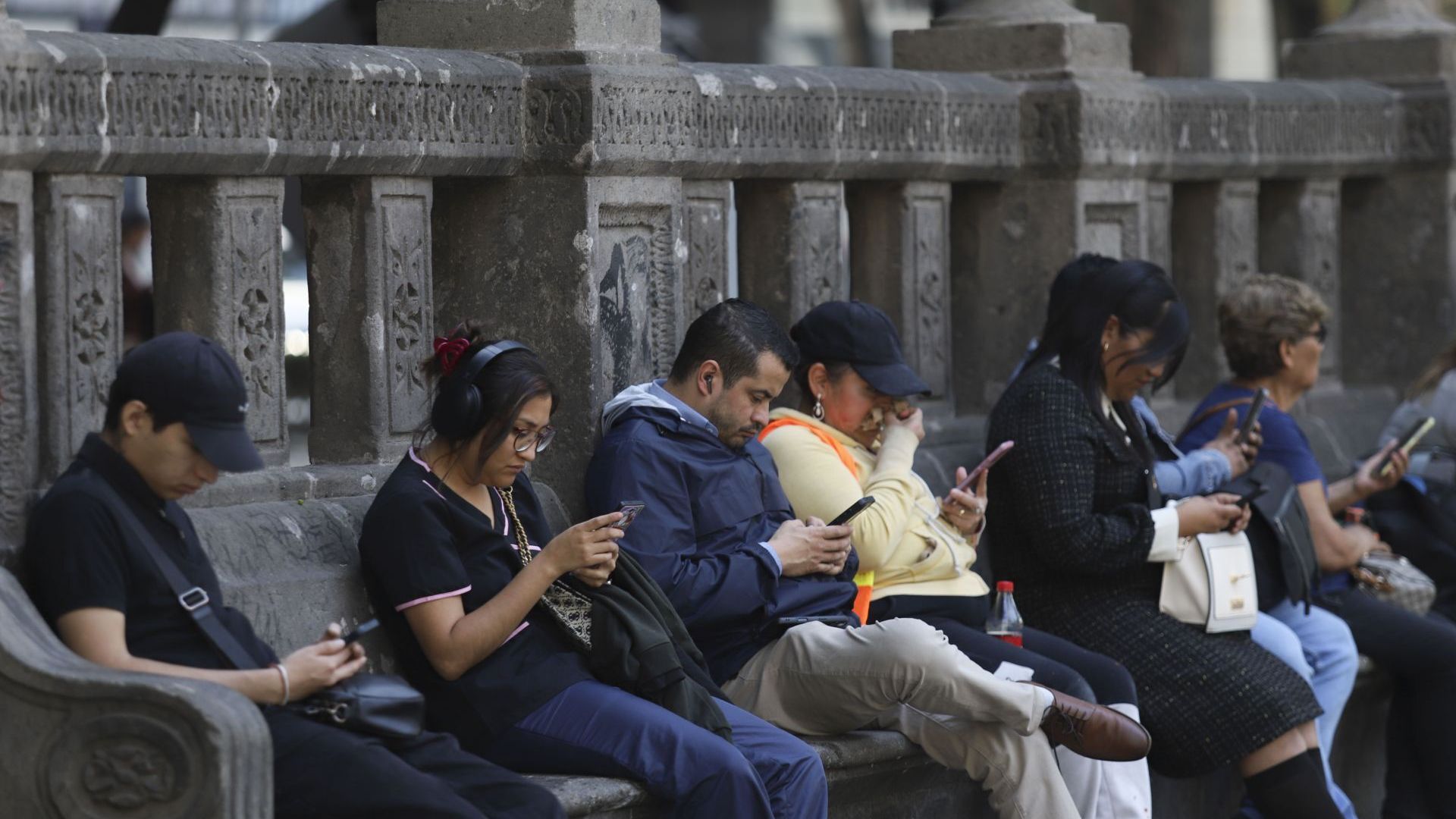 Capitalinos usan el celular mientras descansan en una de las bancas de Avenida Reforma. Foto: Cuartoscuro